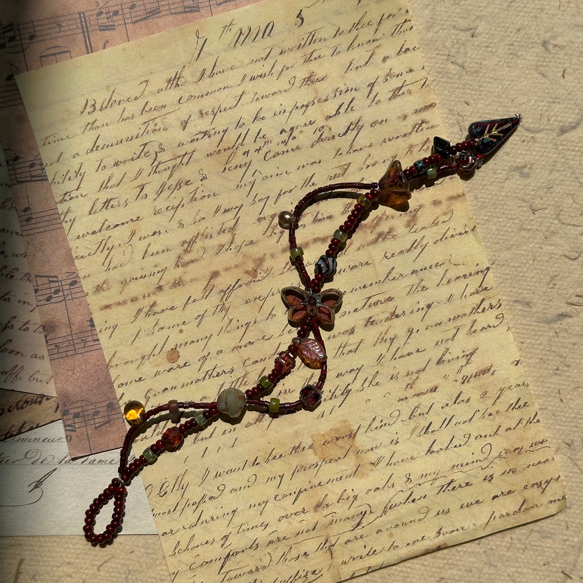 Midnight Butterfly Shadow Bracelet flat-lay on vintage script paper, crimson butterfly centerpiece with autumn leaf and glass accents