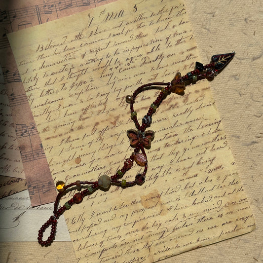 Midnight Butterfly Shadow Bracelet flat-lay on vintage script paper, crimson butterfly centerpiece with autumn leaf and glass accents