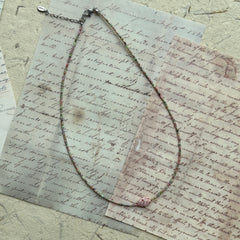 Delicate beaded necklace looped on paper background, minimalist strand of pastel seed beads with soft pink flower bead