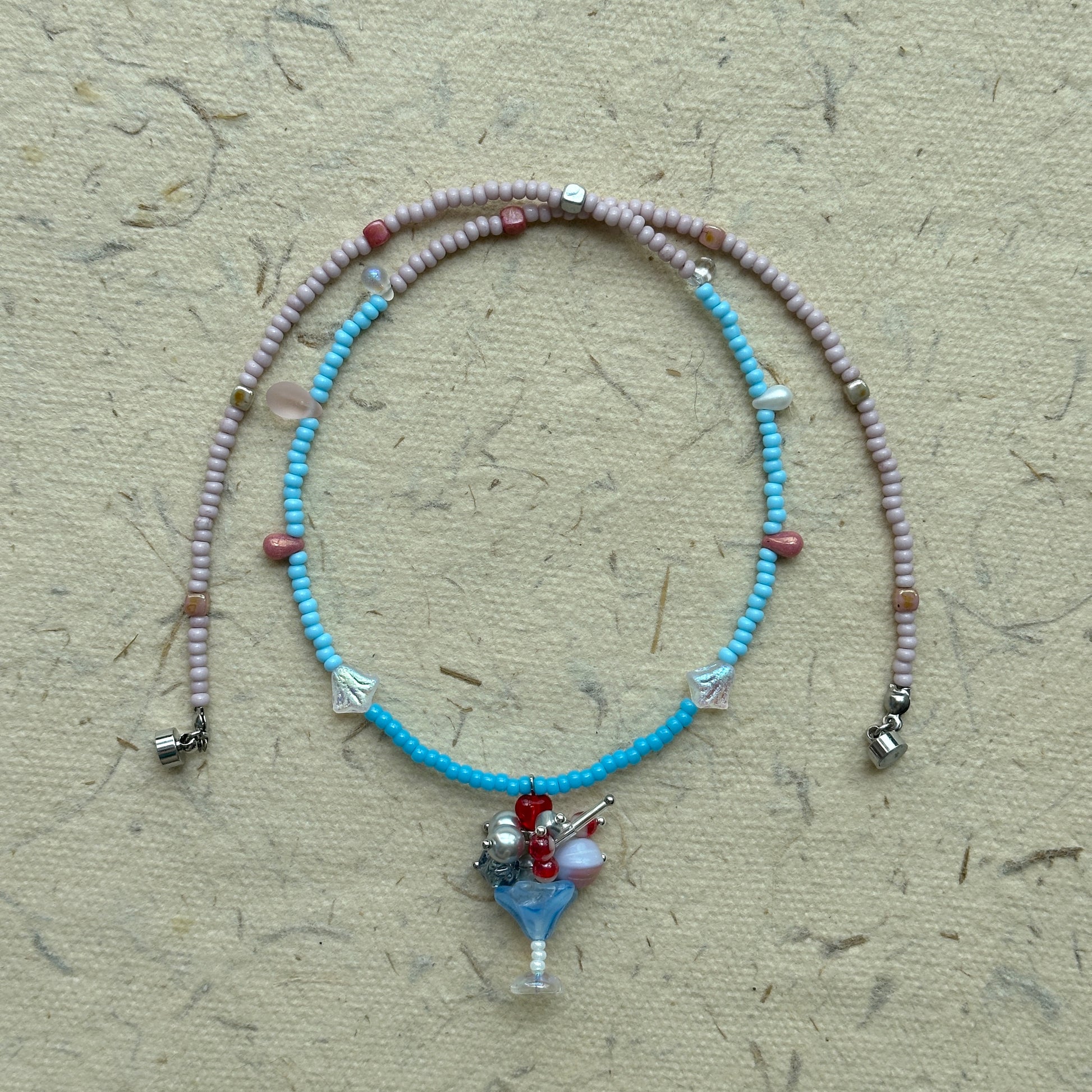 Necklace arranged in a circle, pastel pink and blue strand with floral charm pendant at the center