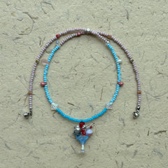 Necklace arranged in a circle, pastel pink and blue strand with floral charm pendant at the center