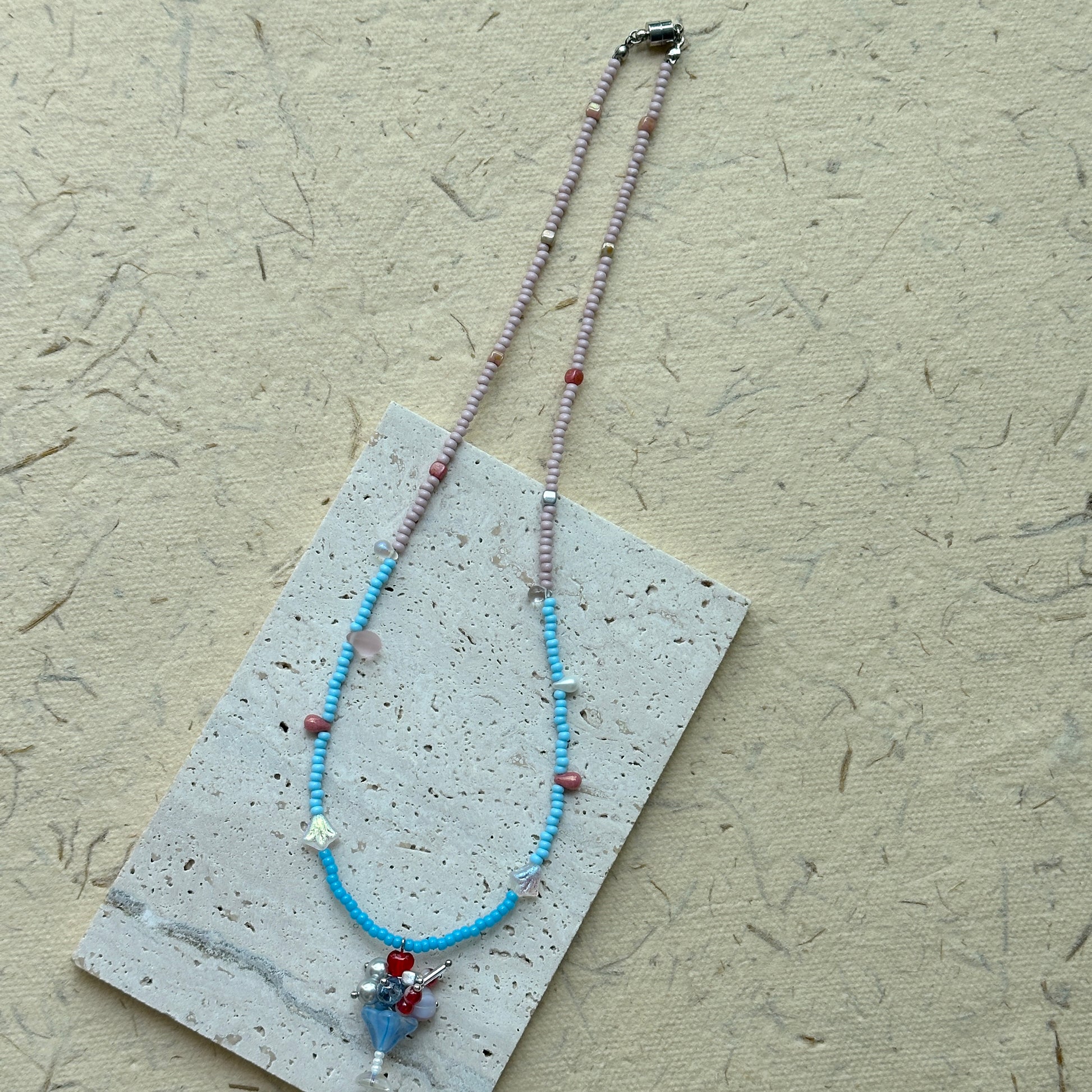 Delicate beaded necklace on card, sky-blue and blush seed beads with whimsical glass blossom and crystal details