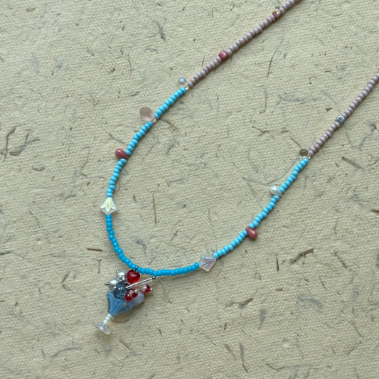 Sky Blossom Charm Necklace flat-lay on fabric, two-tone seed beads in powder pink and sky blue with floral cluster pendant