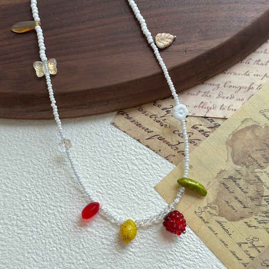Fruit Garden Necklace with white seed beads and colorful fruit charms on display stand