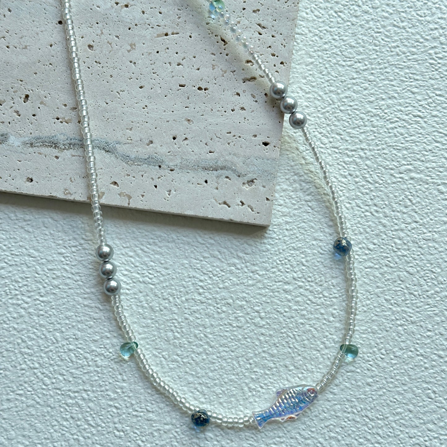 Azure Fish Necklace with iridescent fish charm on textured display