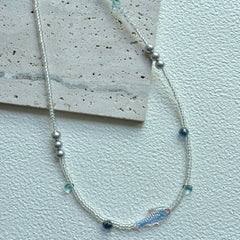 Azure Fish Necklace with iridescent fish charm on textured display