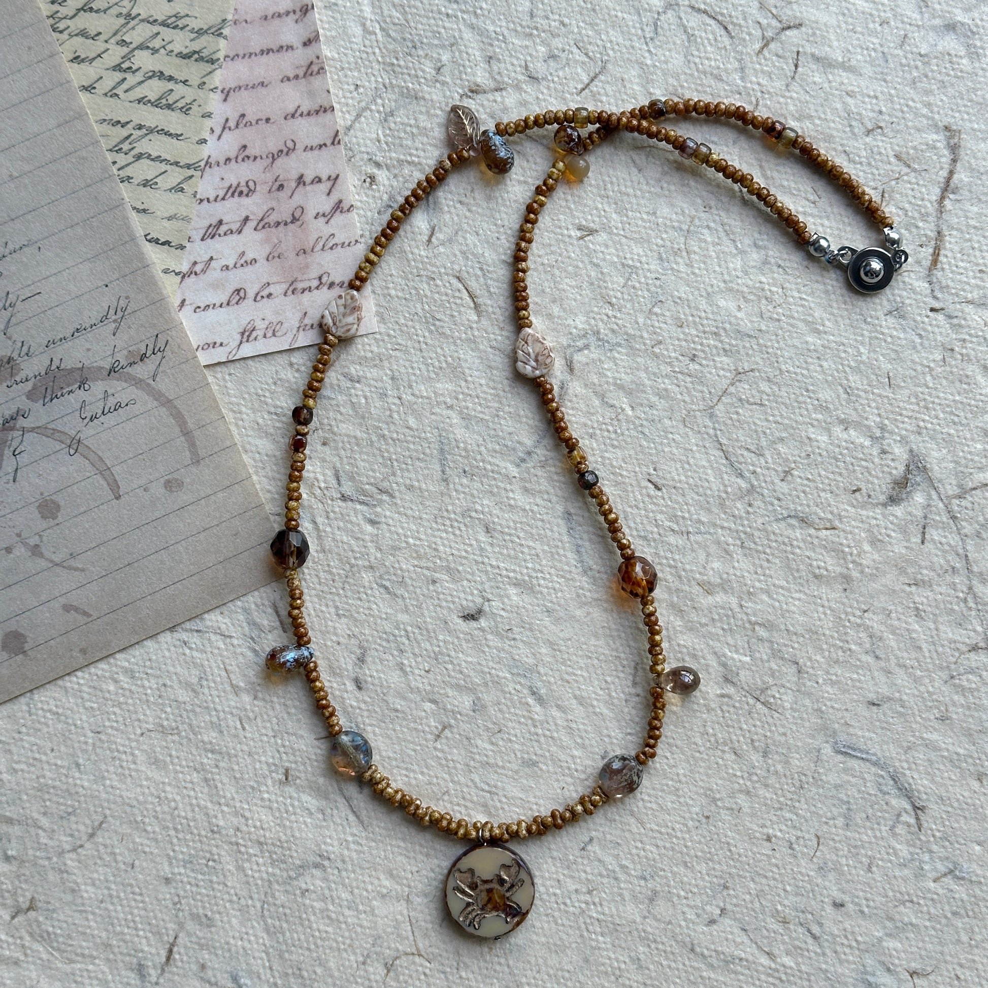 Close-up of crab motif round pendant with earthy brown beads
