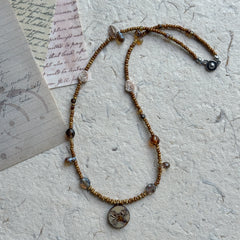 Close-up of crab motif round pendant with earthy brown beads