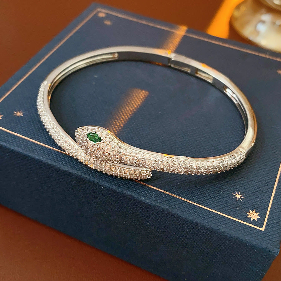 Gold and silver snake-shaped zircon bangles with emerald eyes — Serpent Luxe Bangle by Glazenya.