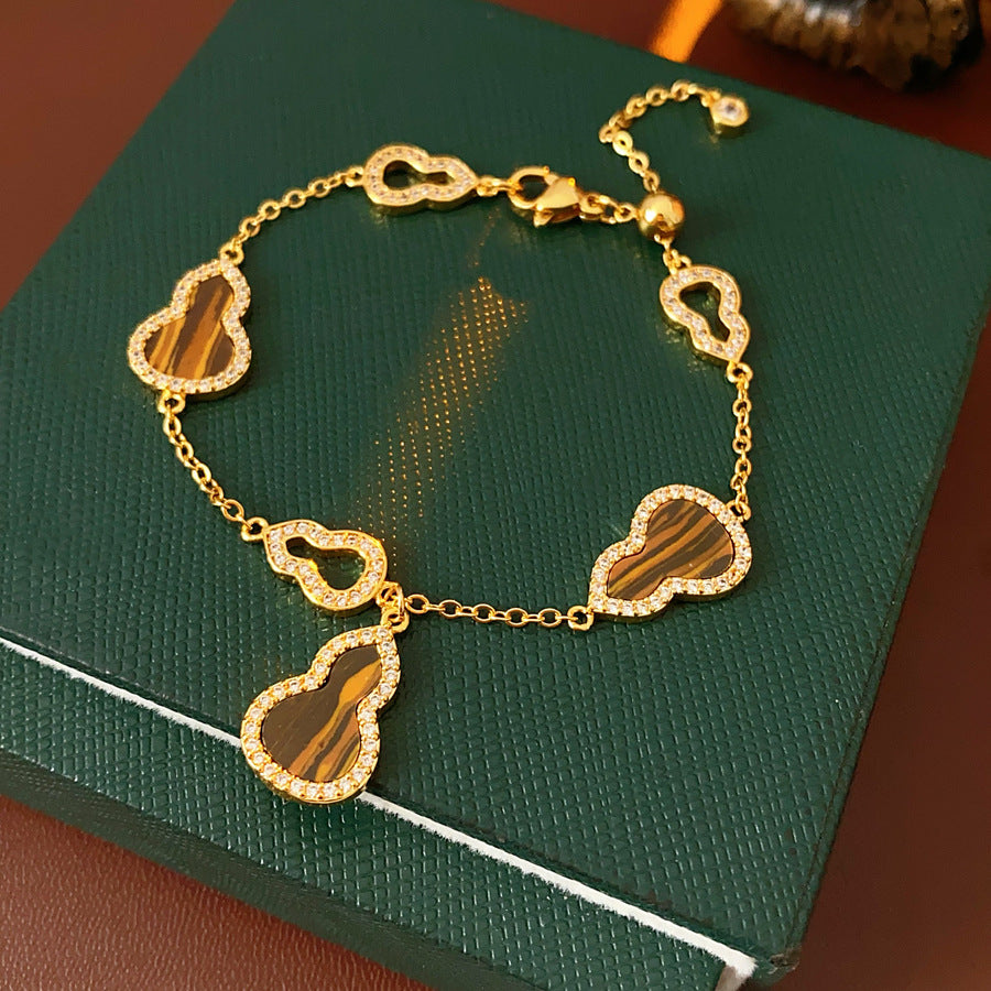 Fortune Gourd Tiger Eye Bracelet with golden gourd motifs, cubic zirconia accents, and natural tiger eye stones, displayed on red wood background
