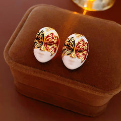 Enamel masquerade face stud earrings with red and black halves and gold filigree on a velvet jewelry box — Venetian Masquerade Studs.