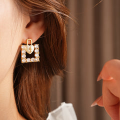Enamel heart-lock and rhinestone square padlock mismatched stud earrings in gold tone.