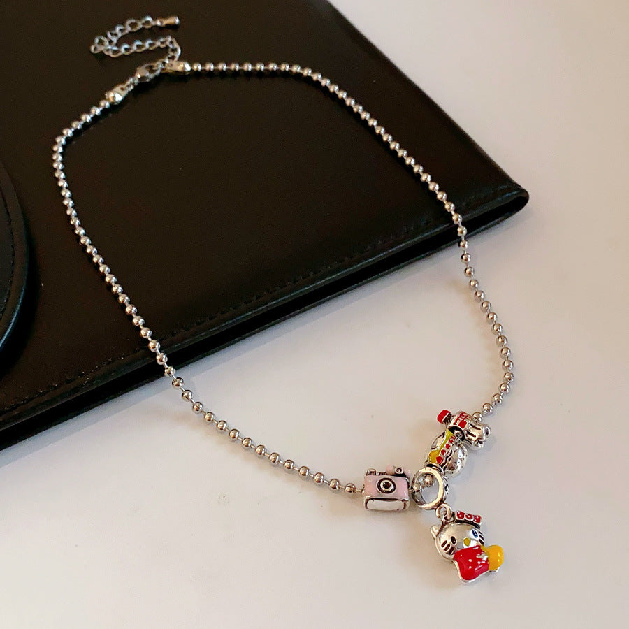 City Voyager Cat Charm Necklace — silver-tone ball chain with enamel cat and camera charms, travel-inspired charm cluster on black pouch