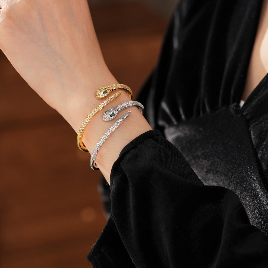 Gold and silver snake-shaped zircon bangles with emerald eyes — Serpent Luxe Bangle by Glazenya.