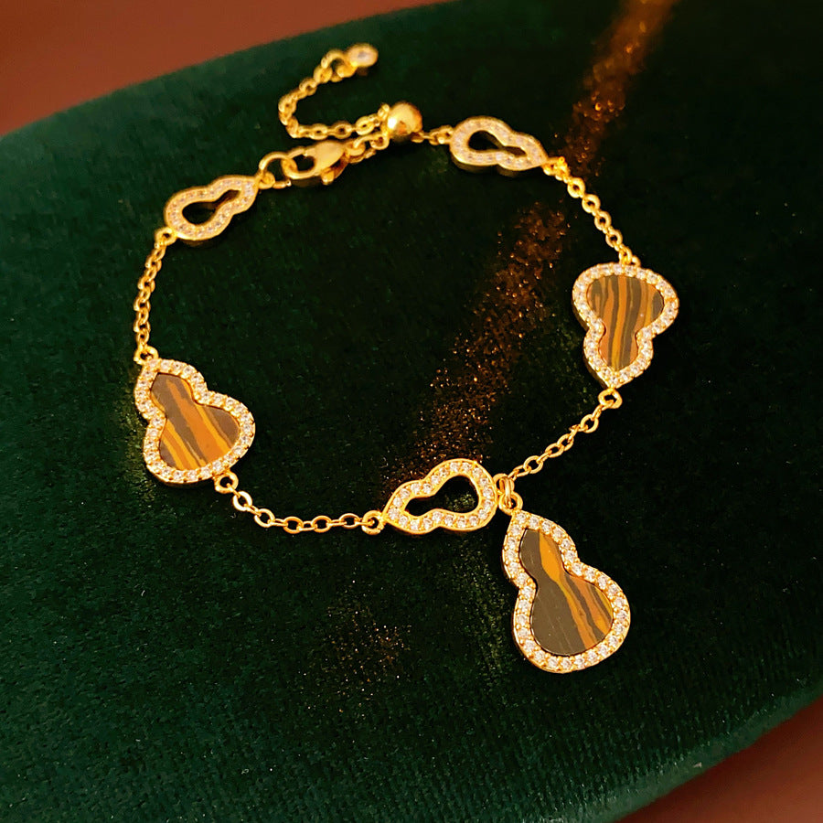 Fortune Gourd Tiger Eye Bracelet with golden gourd motifs, cubic zirconia accents, and natural tiger eye stones, displayed on red wood background