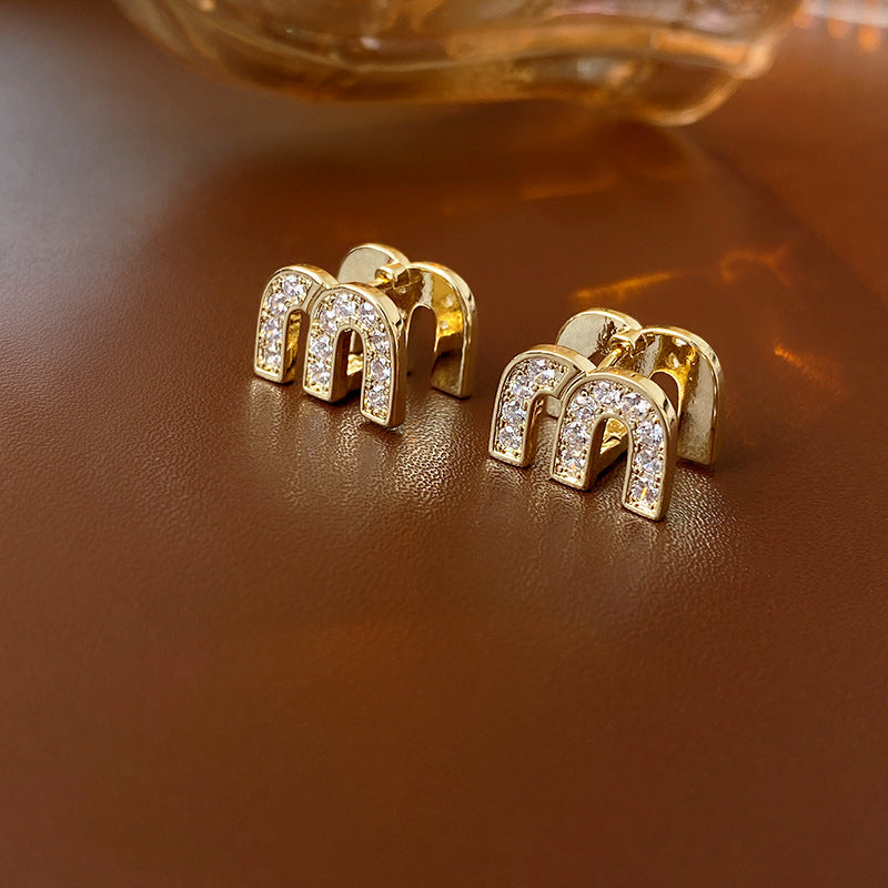 Gold arc “M” stud earrings in pavé crystal and white enamel — Muse Arc Pavé Stud Earrings.