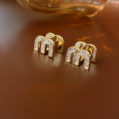 Gold arc “M” stud earrings in pavé crystal and white enamel — Muse Arc Pavé Stud Earrings.