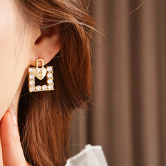 Enamel heart-lock and rhinestone square padlock mismatched stud earrings in gold tone.