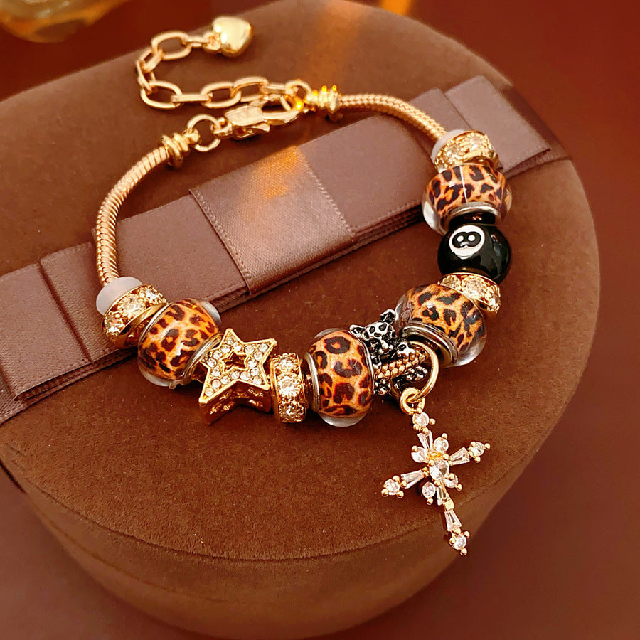 Leopard Cross Luxe Bracelet with leopard-patterned beads, zircon accents, black 8-ball bead, and cross pendant on gold chain