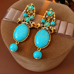 Gold filigree earrings with large turquoise cabochons, crystal accents, and dangling bead — Azure Oasis Turquoise Earrings.