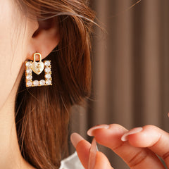 Enamel heart-lock and rhinestone square padlock mismatched stud earrings in gold tone.