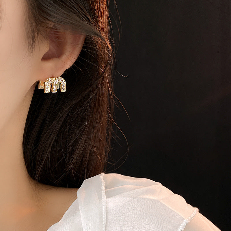 Gold arc “M” stud earrings in pavé crystal and white enamel — Muse Arc Pavé Stud Earrings.