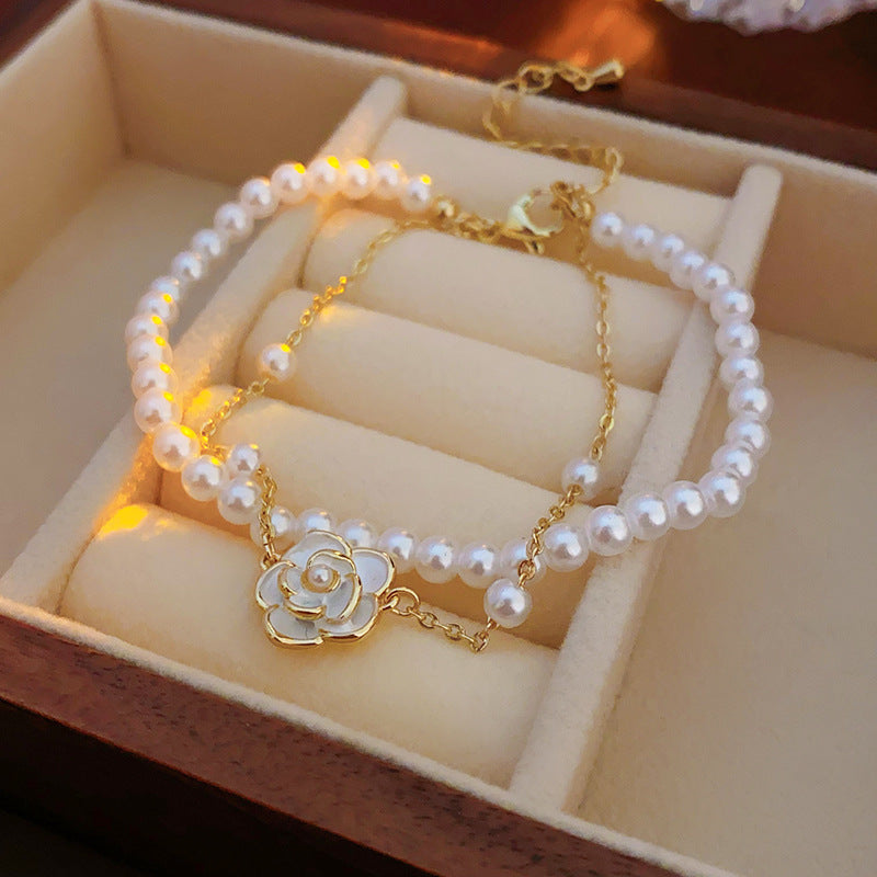 Layered faux-pearl bracelet with gold-tone chain and white enamel flower charm placed in a green jewelry tray — Petite Pearl Bloom Layered Bracelet.