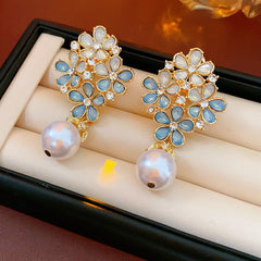 Gold floral cluster earrings with ice-blue petals, crystal accents, and a single luminous faux-pearl drop — Ethereal Petal Pearl Earrings.