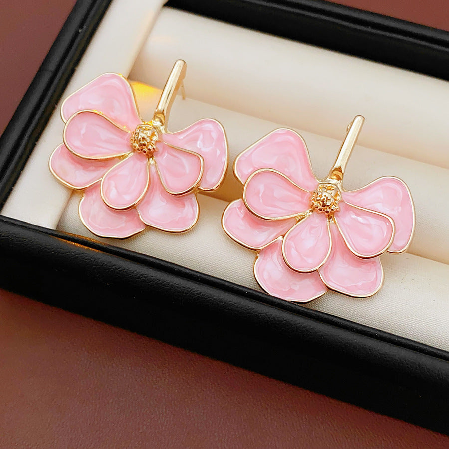 Close-up of pink enamel flower earrings with gold tone petals, statement design on jewelry tray
