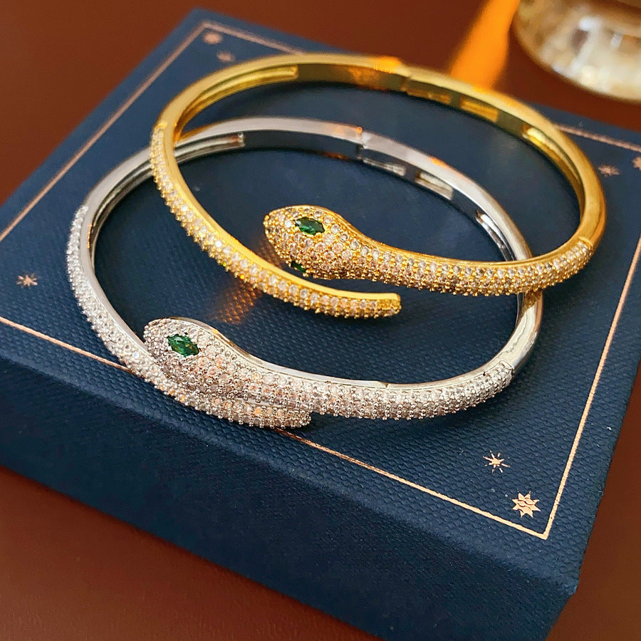 Gold and silver snake-shaped zircon bangles with emerald eyes — Serpent Luxe Bangle by Glazenya.