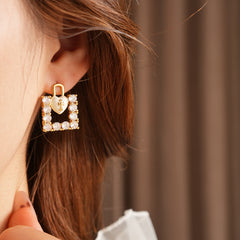 Enamel heart-lock and rhinestone square padlock mismatched stud earrings in gold tone.