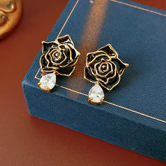 Gold-tone rose stud earrings with ivory and black enamel petals plus teardrop zircon dangles — Gilded Rose Teardrop Studs.