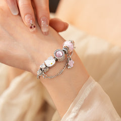 Rosy Pawprints Charm Bracelet — silver-tone snake chain with pink crystal bezel, checker enamel bead, cat-with-bow, paw and bone charms in jewelry tray