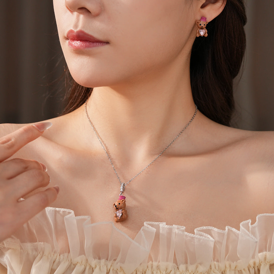 Silver-tone necklace with coffee teddy pendant and pink hat, matching teddy stud earrings with heart crystal — Sweetheart Teddy Crystal Jewelry.