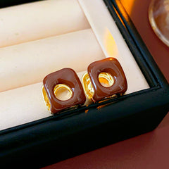 Square pillow ear cuffs with glossy enamel shell and mirrored gold core in white, red, and coffee — Gilded Core Pillow Ear Cuffs.