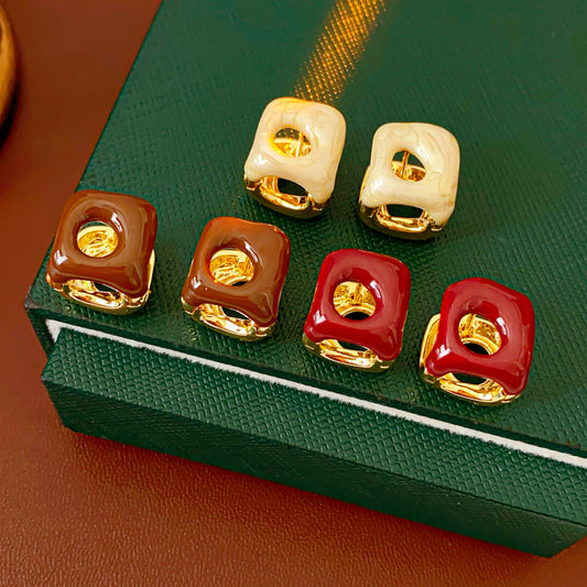 Square pillow ear cuffs with glossy enamel shell and mirrored gold core in white, red, and coffee — Gilded Core Pillow Ear Cuffs.