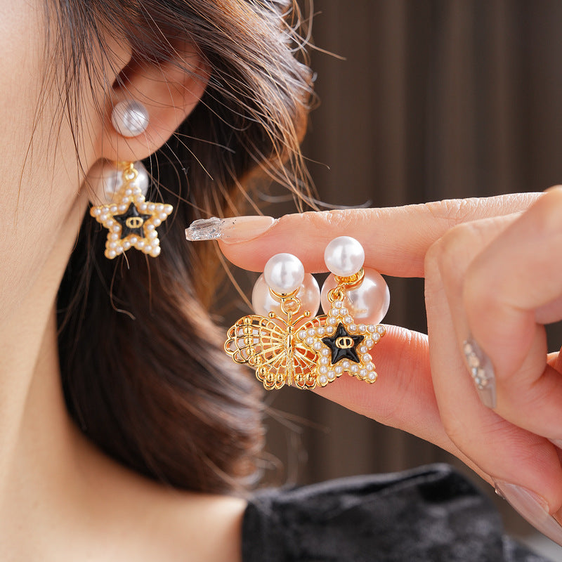 Double-pearl stud earrings with gold-tone butterfly and star charms displayed in a jewelry tray — Double Pearl Charm Studs.