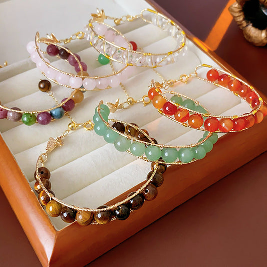 Natural stone beaded bracelets in multiple colors including red agate, rose quartz, and white crystal, with golden accents displayed in a jewelry tray.