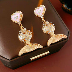 Gold-tone mermaid tail drop earrings with pink enamel heart studs and rhinestone accents on a green velvet background