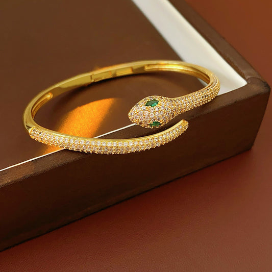 Gold and silver snake-shaped zircon bangles with emerald eyes — Serpent Luxe Bangle by Glazenya.