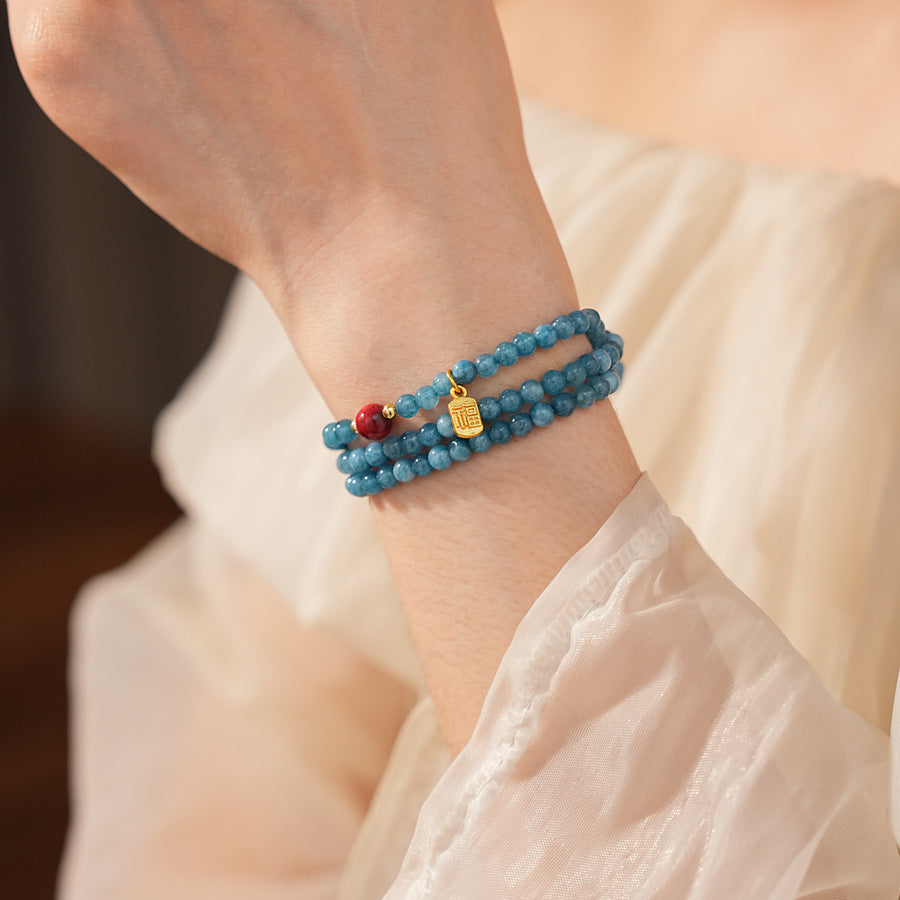 Blue multi-wrap beaded bracelet with red accent bead and gold charm — Azure Charm Wrap Bracelet.