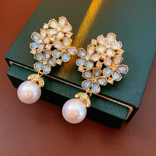 Gold floral cluster earrings with ice-blue petals, crystal accents, and a single luminous faux-pearl drop — Ethereal Petal Pearl Earrings.