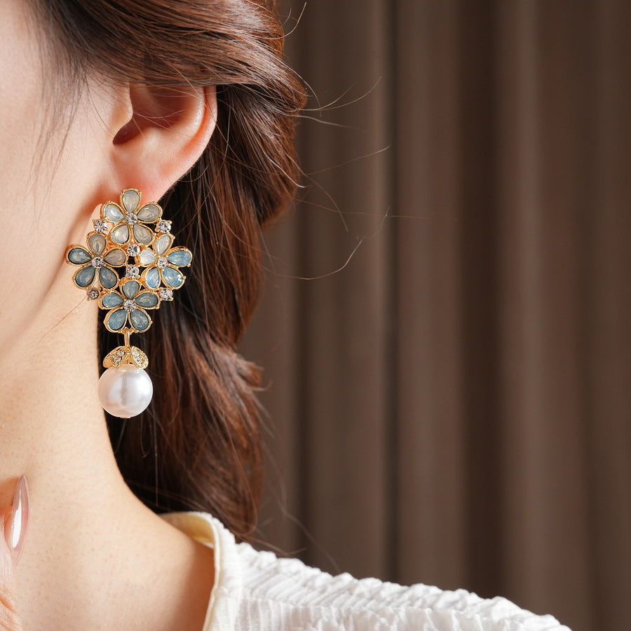 Gold floral cluster earrings with ice-blue petals, crystal accents, and a single luminous faux-pearl drop — Ethereal Petal Pearl Earrings.