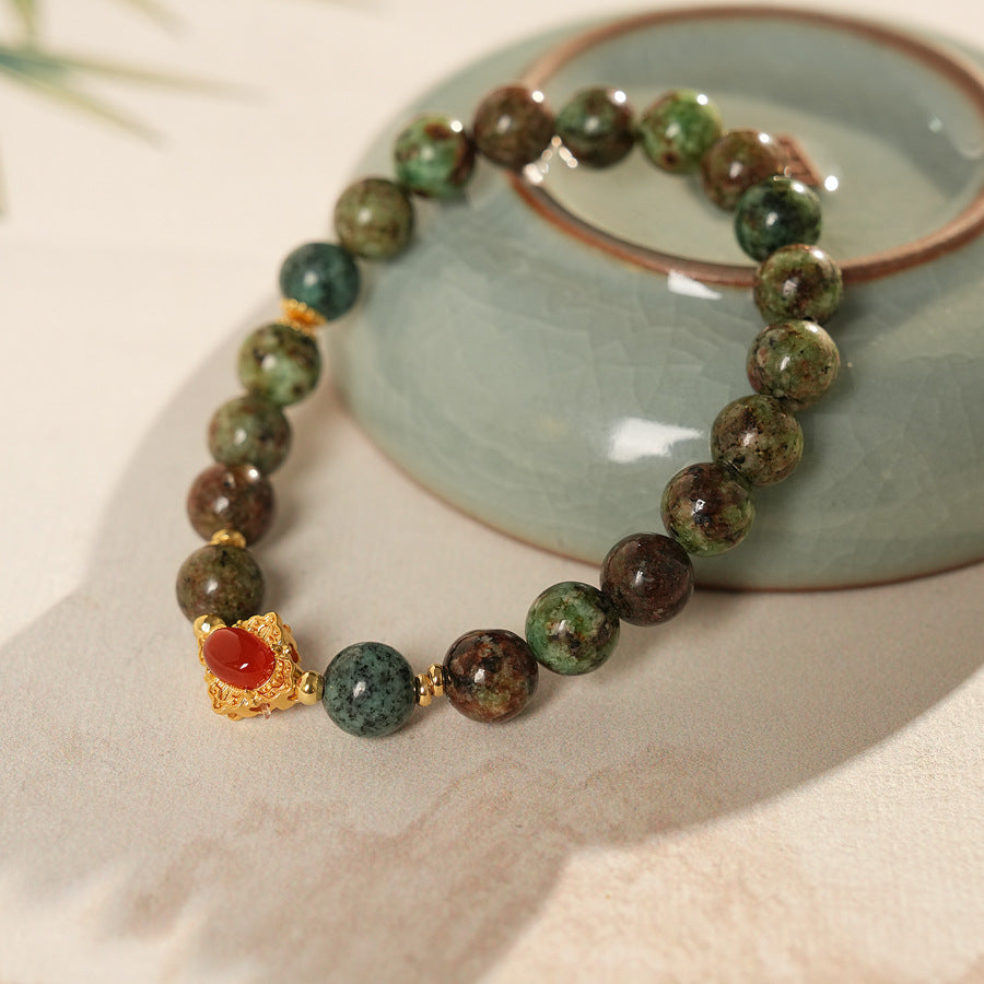 <div class="gz-desc">
  <p>Earthy and refined <strong>natural stone bracelet</strong> combining lush <strong>green ghost</strong> beads with smooth <strong>agate</strong>, accented by a warm red centerpiece and gold-tone spacers for a subtle touch of luxury.</p>

  <h3>Design Story</h3>
  <p>The <strong>Forest Ember Agate Bracelet</strong> evokes the calm of an ancient forest lit by a single ember. Mossy green tones bring grounding energy, while the red accent adds a gentle spark—balance between serenity an