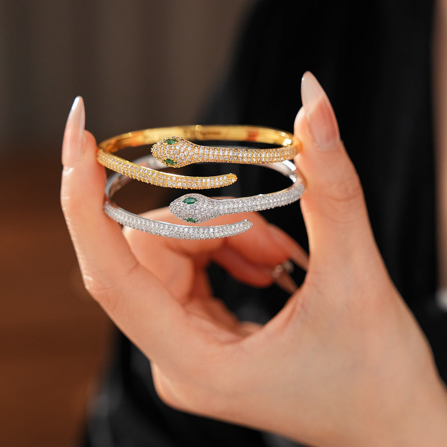 Gold and silver snake-shaped zircon bangles with emerald eyes — Serpent Luxe Bangle by Glazenya.