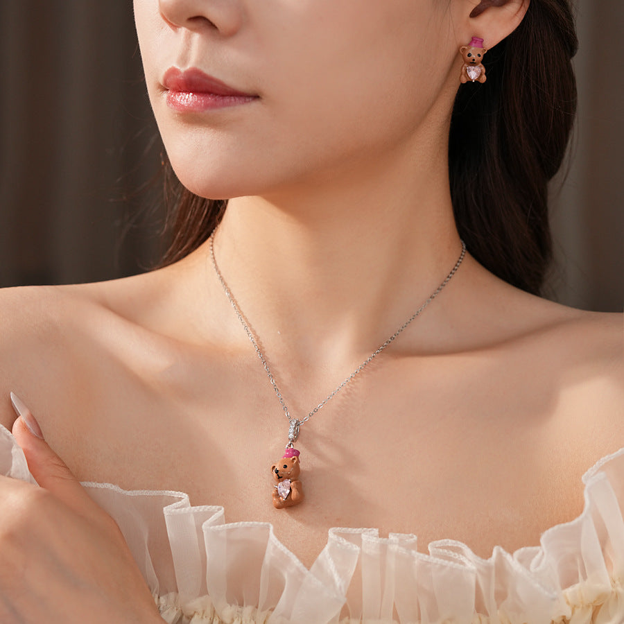 Silver-tone necklace with coffee teddy pendant and pink hat, matching teddy stud earrings with heart crystal — Sweetheart Teddy Crystal Jewelry.