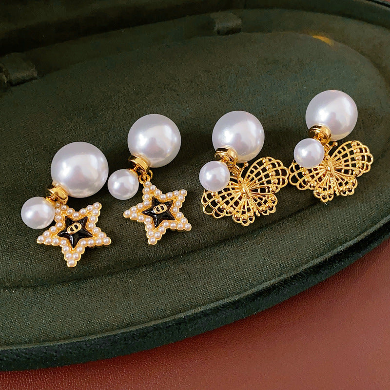Double-pearl stud earrings with gold-tone butterfly and star charms displayed in a jewelry tray — Double Pearl Charm Studs.