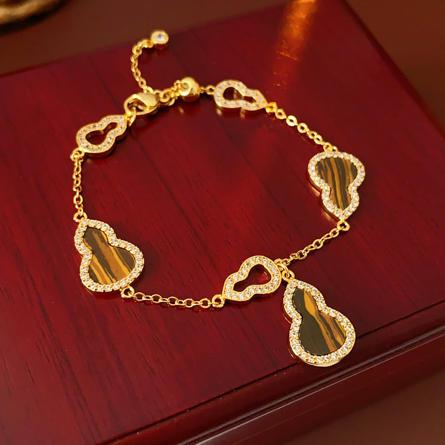 Fortune Gourd Tiger Eye Bracelet with golden gourd motifs, cubic zirconia accents, and natural tiger eye stones, displayed on red wood background