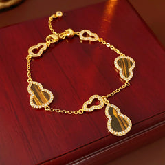 Fortune Gourd Tiger Eye Bracelet with golden gourd motifs, cubic zirconia accents, and natural tiger eye stones, displayed on red wood background