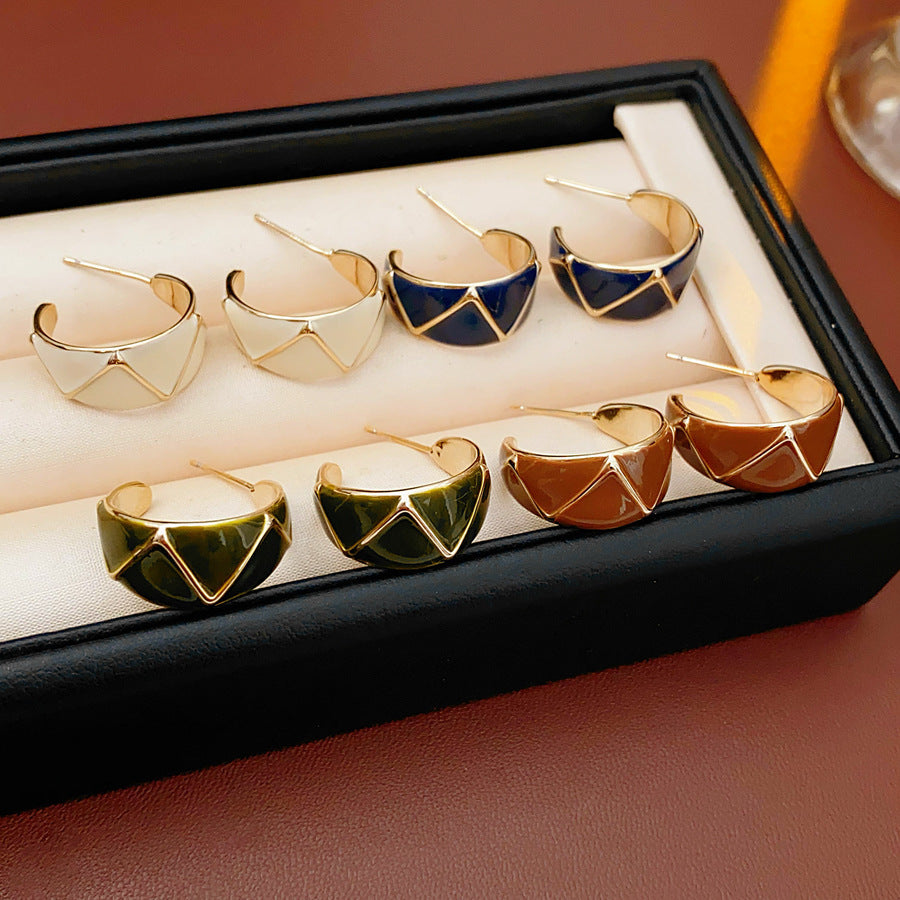 Set of four geometric enamel hoop earrings in white, blue, coffee, and green displayed in a jewelry tray